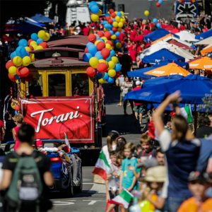 A balloon-decorated cable car leading the Italian Heritage Parade through a crowded San Francisco street