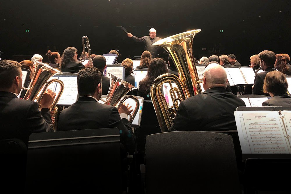 Conductor Pete Nowlen leads the Concert Band on stage, tubas and brass players in the foreground.