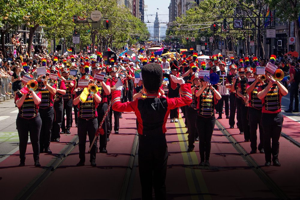 San Francisco Pride Band marches down Market Street during the SF Pride Parade, led by a drum major with arms raised.